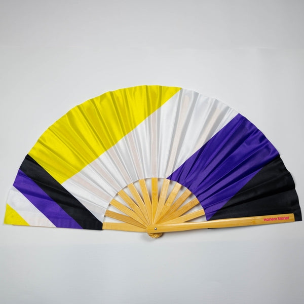 A Bamboo & Silk handheld folding fan that is yellow, white, purple and black in a non binary flag print, is spread open on a white background.