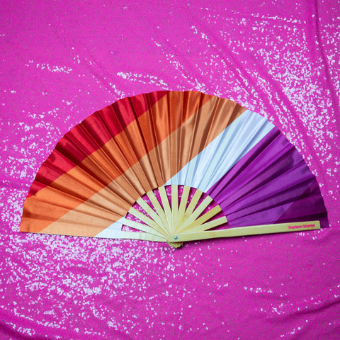 Bamboo clack fan featuring a vibrant Lesbian flag design on a pink glitzy background, perfect for pride and festivals.