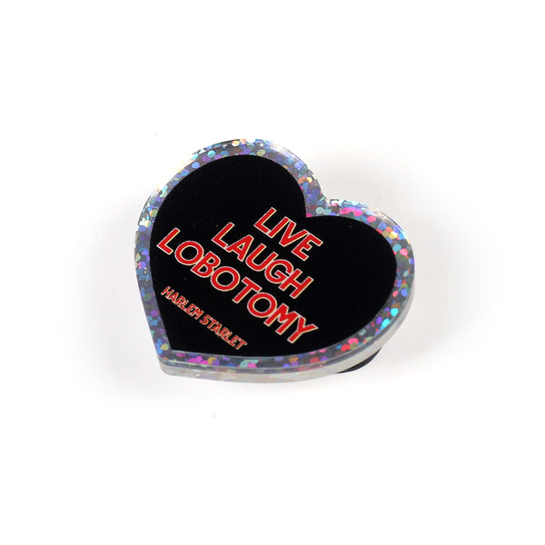 Heart pin with a black background, featuring red text that says "Live, Laugh, Lobotomy". Edges are silver with multicolored glitter. Mental Health Pins.