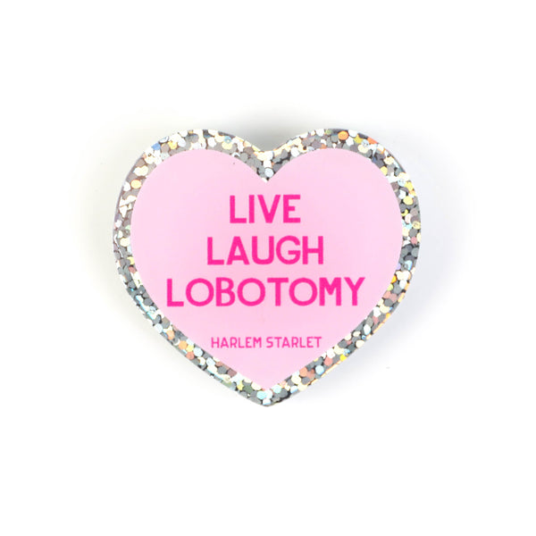 Heart pin with a pink background, featuring hot pink text that says "Live, Laugh, Lobotomy". Edges are silver with multicolored glitter. Mental Health Pins.