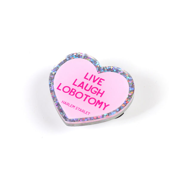 Heart pin with a pink background, featuring hot pink text that says "Live, Laugh, Lobotomy". Edges are silver with multicolored glitter. Mental Health Pins.