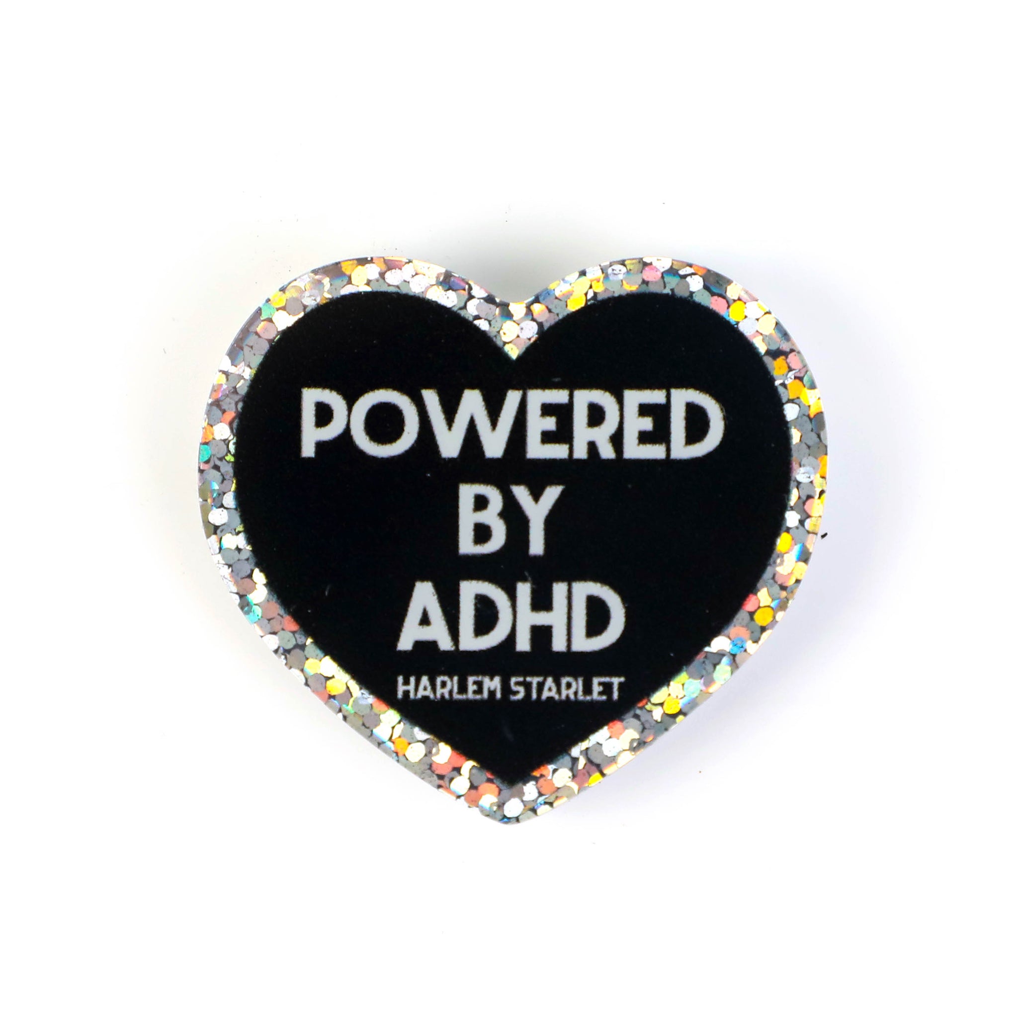 Heart pin with a black background, featuring white text that says "Powered by ADHD!". Edges are silver with multicolored glitter. Neurodivergent Pride Pin.