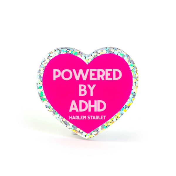 Heart pin with a hot pink background, featuring light pink text that says "Powered by ADHD!". Edges are silver with multicolored glitter. Neurodivergent Pride Pin.