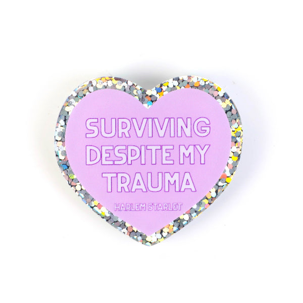 featuring white text that says "Surviving Despite My Trauma". Edges are silver with multicolored glitter.